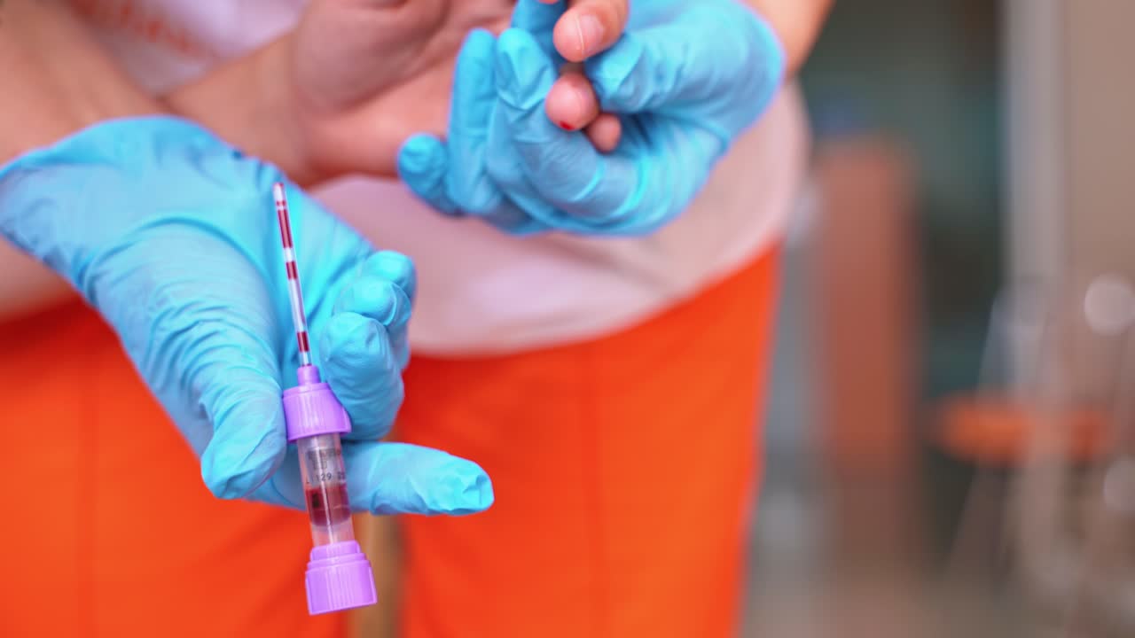 Close-up nurse's hands collecting blood. Medical assistant in blue sterile gloves is taking blood samples from finger. Healthcare concept.