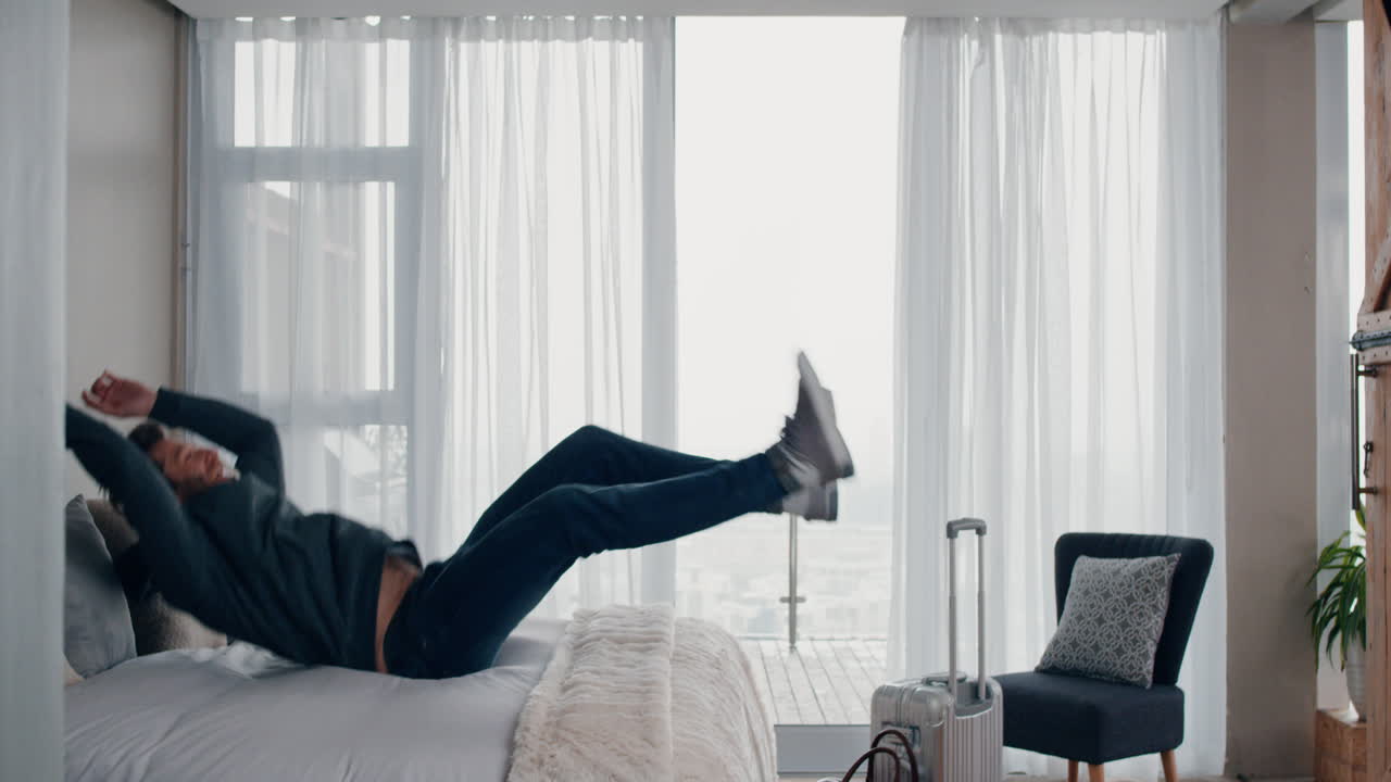 행복한 젊은이가 침대에 뛰어들고 성공적인 여행 여행 후 휴식을 취하고 독립적인 생활 방식의 자유를 즐기고 있습니다.