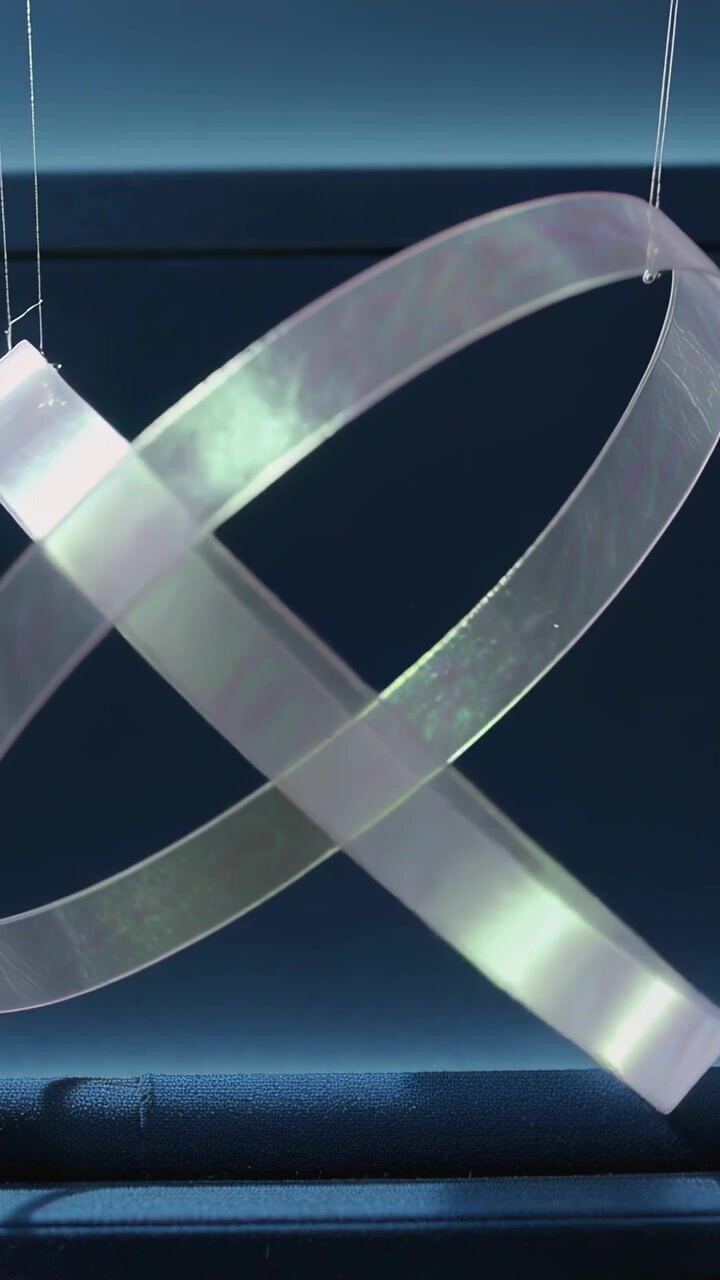 Vertical video: Swinging double-loop ribbon being nudged on strings near navy panel with clear bead