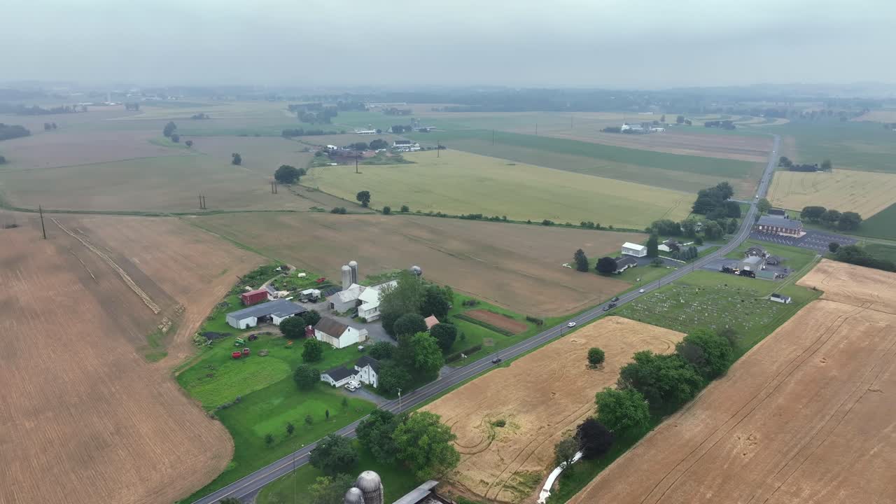 American farmstead with silo and cars on street during foggy and rainy day. Aerial top down shot. Cloudy day in United States of America.wide shot.