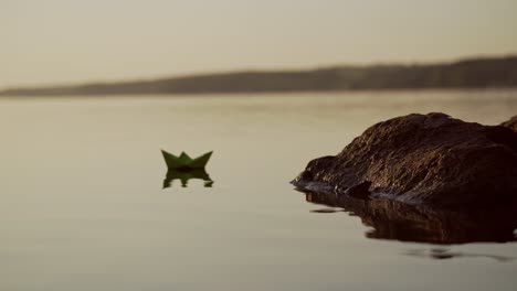green paper ship in the river. origami paper boat is sailing in the lake. beautiful waves ripple background. unusual travel concept. filtered video.