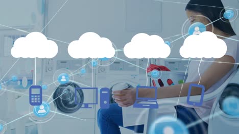 Animation-of-network-of-connections-with-clouds-over-biracial-woman-using-smartphone-at-laundry