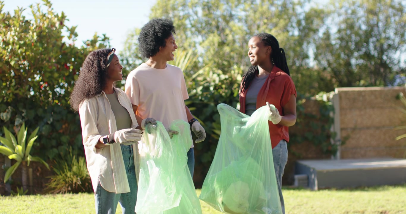 African friends lifting and inspecting green bags showing litter with gloves in yard after cleanup