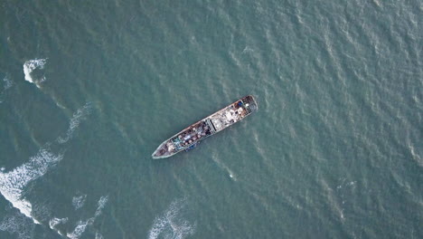 Aerial top orbit lowering view over wreckage of ship in Dharmadam, India