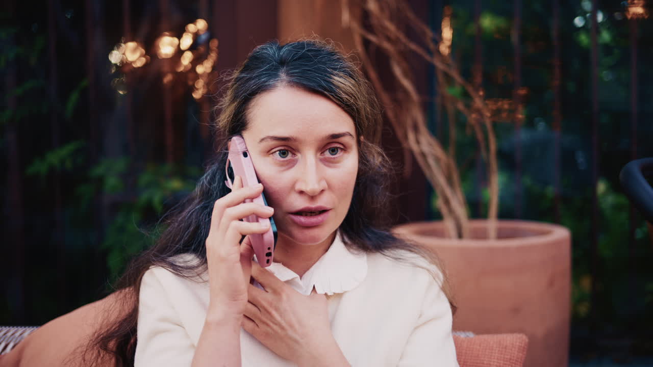 Woman sitting outdoors while talking on a smartphone, looking thoughtful