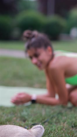 un cachorro de pug jugando al aire libre con una mujer practicando yoga
