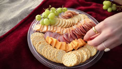 Woman's-hand-takes-cheese-slice-from-beach-picnic-platter,-slow-motion-close-up-zoom-in