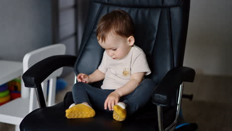 little cute toddler boy sits in a big office chair. baby looks at his seat carefully with interest touching leather cover.