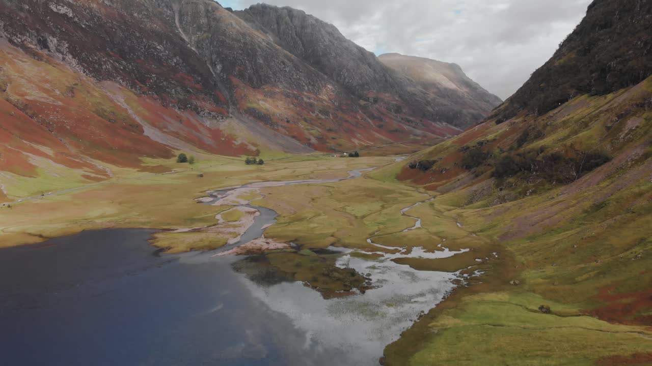 descendiendo lentamente hacia un valle de tierras altas en el área de glencoe de escocia, volando sobre un tranquilo lago escocés rodeado de montañas