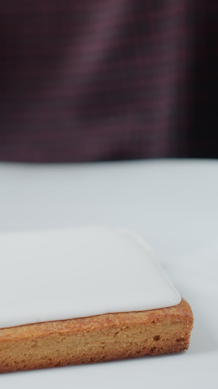 primer plano de un panadero cubriendo cuidadosamente una galleta en una placa de cerámica blanca, un glaseado blanco liso se aplica con precisión, una persona con ropa a cuadros se centra en decorar la galleta