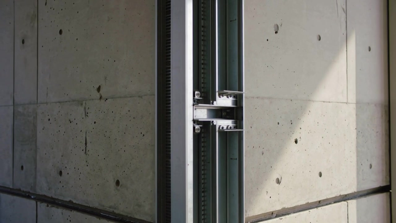 Telecamera in movimento che rivela un canale metallico verticale nel corridoio, esponendo una cremagliera dentata per l'ispezione