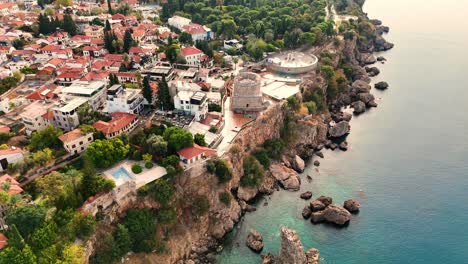 a stunning aerial view of antalya old town, turkey, showcasing the rocky coastline, turquoise waters, terracotta rooftops, roman-era landmarks, and the iconic hidirlik tower.