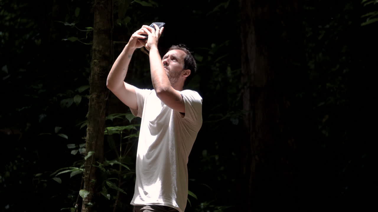 검은 깊은 정글을 배경으로 광야의 자연 환경에서 스마트폰으로 셀카 사진을 찍는 운동 백인 관광객