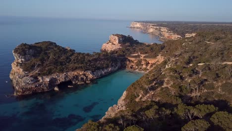 vuelo aéreo de drones que muestra la hermosa bahía de calo des moro con iluminación rocosa de la costa al atardecer en la isla de mallorca - mar mediterráneo de fondo por la noche