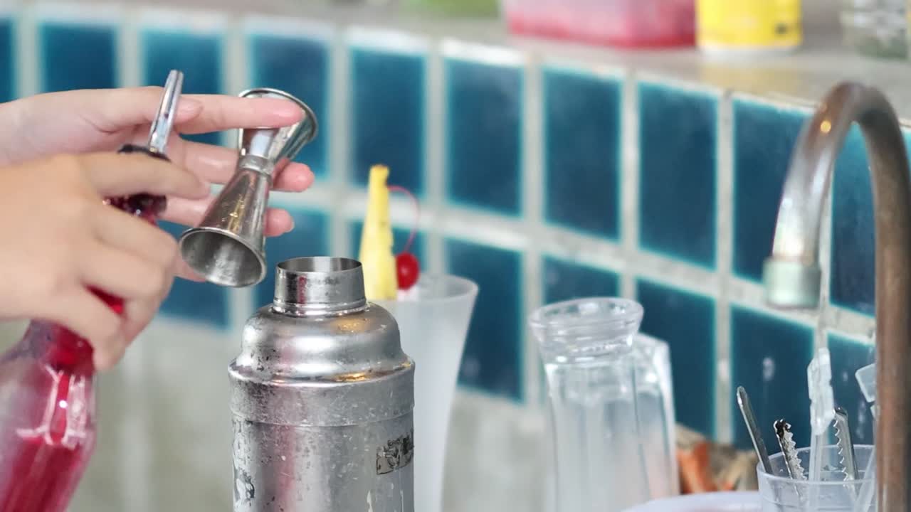 Un barman utiliza un medidor para medir y verter sirope rojo en una coctelera