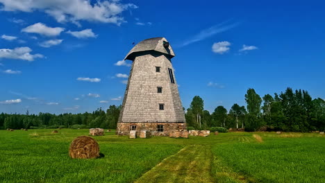 historic wooden windmill in a green field with a hay bale under a blue sky