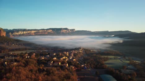 Vilanova-de-sau-village-in-spain-with-morning-fog-and-mountains-in-the-background,-aerial-view