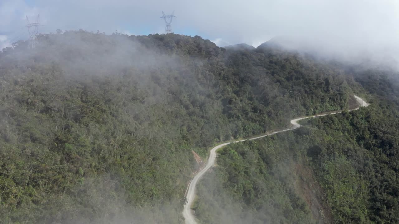 un camino de grava cortado en lo alto de una empinada selva nublada en la ladera de una montaña en bolivia