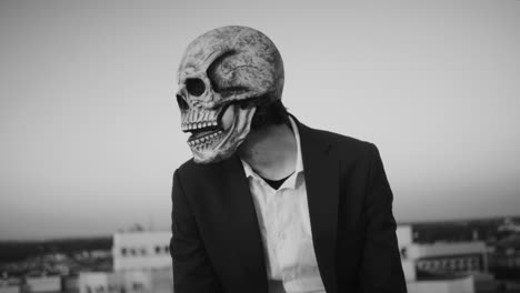 person in skull mask wearing a suit on a rooftop in black and white