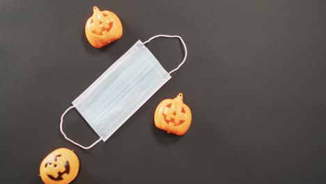 Three-halloween-pumpkin-toys-and-face-mask-against-grey-background