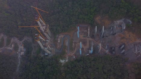 industrial crane towers in expressway road construction site, sahyadri mountains and forest, mumbai pune expressway construction site, lonavala, maharashtra, revealing drone shot