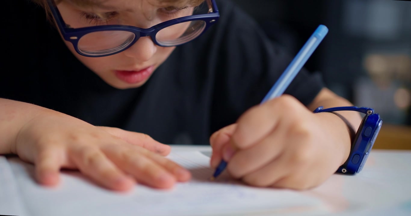 Bambino concentrato con gli occhiali che scrive su un quaderno