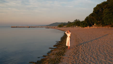 A-young-girl-stands-by-the-seaside,-facing-the-rising-sun,-shielding-her-eyes-with-her-hands-from-the-rays-of-sunlight