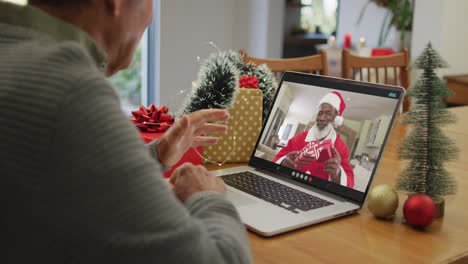 Un-Hombre-Mayor-Caucásico-Teniendo-Una-Videollamada-Navideña-En-Una-Computadora-Portátil-Con-Un-Papá-Noel-Afroamericano-En-La-Pantalla