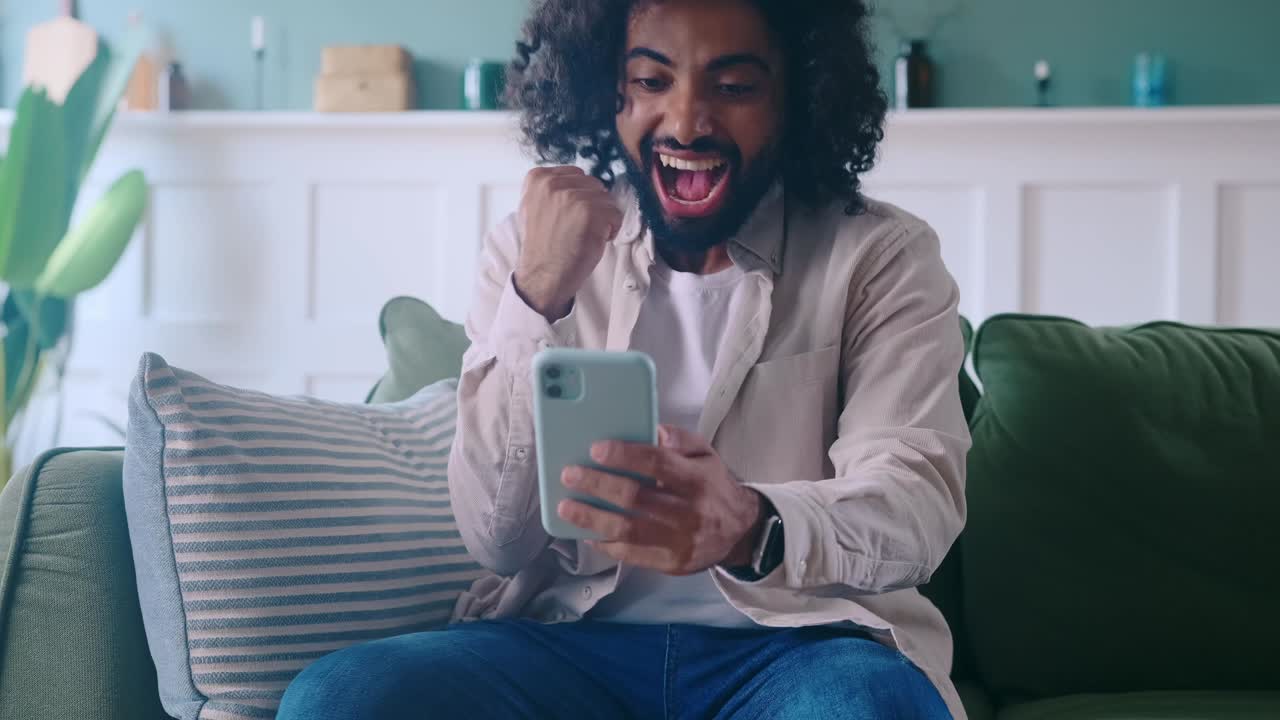 Homem árabe radiante gritando e acenando com as mãos após receber uma mensagem no celular