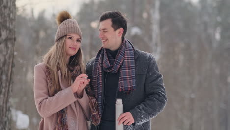 couple in love in the winter forest to drink tea from a thermos. stylish man and woman in a coat in the park in winter for a walk.