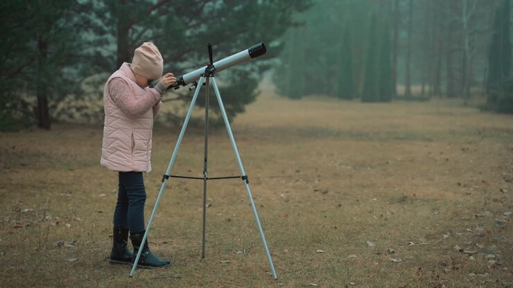 Little girl looking through a telescope in the forest