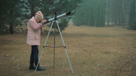 una ragazzina che guarda attraverso un telescopio nella foresta