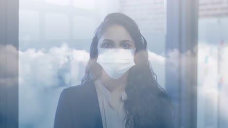 Clouds-in-blue-sky-against-portrait-of-indian-woman-wearing-face-mask-at-office