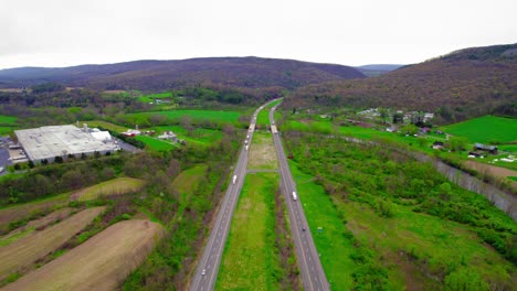 Vista-Aérea-De-La-Autopista-Con-Semirremolques-En-Milesburg,-Pensilvania,-Rodeada-De-Paisajes-Verdes.