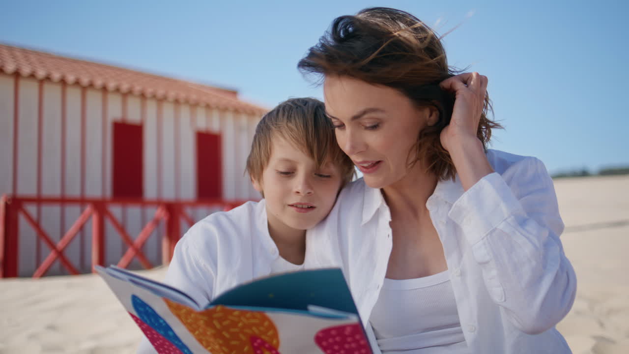Woman reading book son on sunny beach closeup. Happy boy listening fairy tale