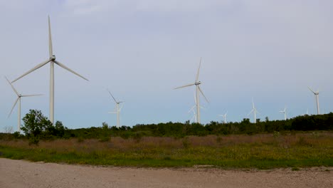 Electrical-renewable-energy-wind-turbines-in-Estonia-Harjumaa-Europe-that-are-spinning-in-slow-motion-during-the-summer-time-while-the-sun-is-shining-and-nature-is-around-them-in-4K