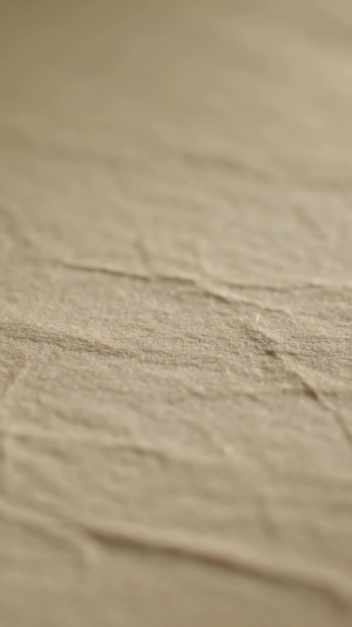 Vertical video: Recording camera initiating focus shift over beige cloth in room, examining weave
