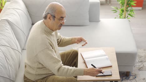 Old-man-looking-at-bills-calculating-with-calculator-at-home.