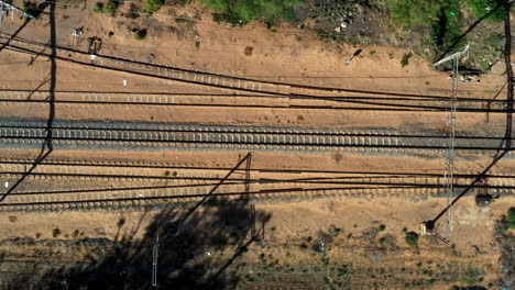 Aerial-drone-shot-of-an-empty-railway-train-track-in-desert-sand-as-a-truck-drives-past-on-the-road-parallel-to-the-tracks