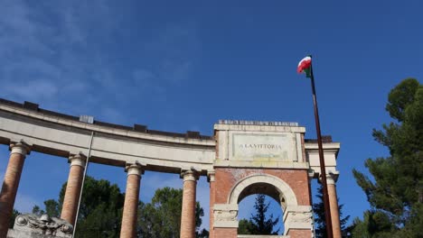 bandera italiana ondeando en el viento - monumento antiguo y cielo azul soleado en el fondo