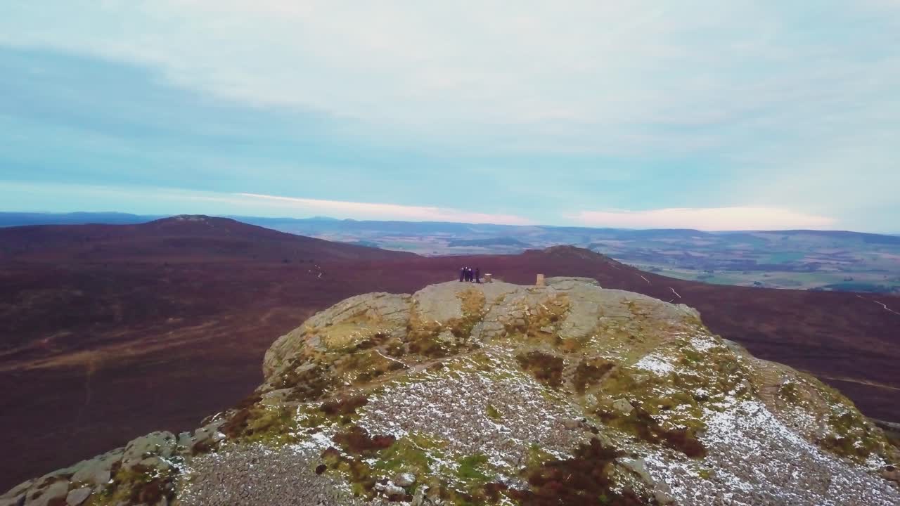 A group of friends standing atop a mountain peak in Scotland, enjoying the view