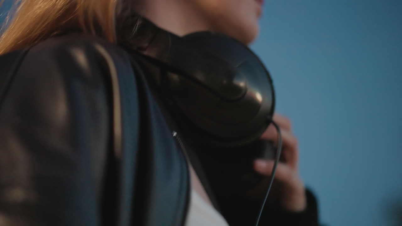 Ung kvinne som lytter, jente med hodetelefoner i skumringen, ung kvinne med øretelefoner som rolig nyter kveldslydene, energisk ung kvinne fordypet i musikk mens hun slapper av på slutten av dagen