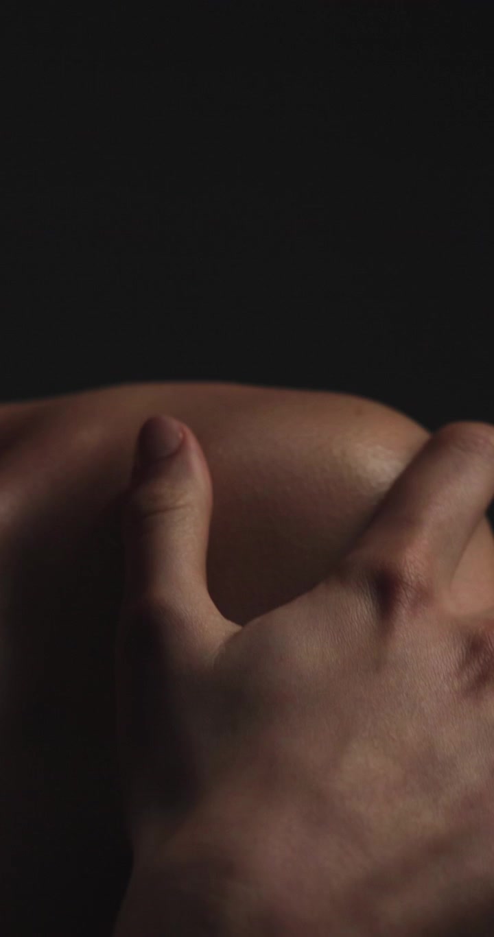 Close-up of Hand Gently Touching Bare Shoulder in Low Light