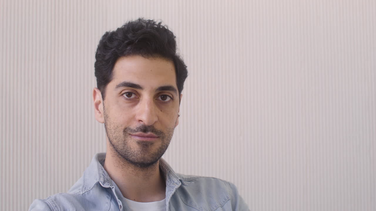 atractivo hombre de cabello oscuro sentado y mirando a la cámara en una habitación