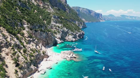 boat tour, tourist people and sandy beach at baunei coast, sardinia, italy - aerial 4k tilting down