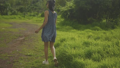 tan woman in dress with short hair walks away along path in forest on sunny day