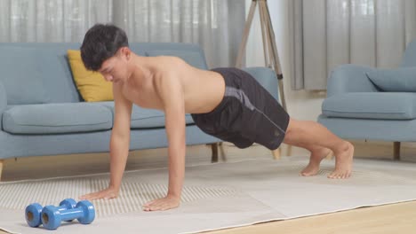 asian teenager boy doing pushups on mat with dumbbells during the shirtless workout at home