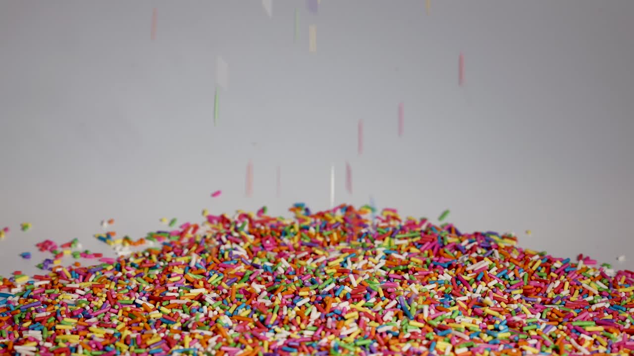 Vibrant sprinkles cascade onto a growing pile against a neutral background, captured in slow motion for a dynamic visual effect