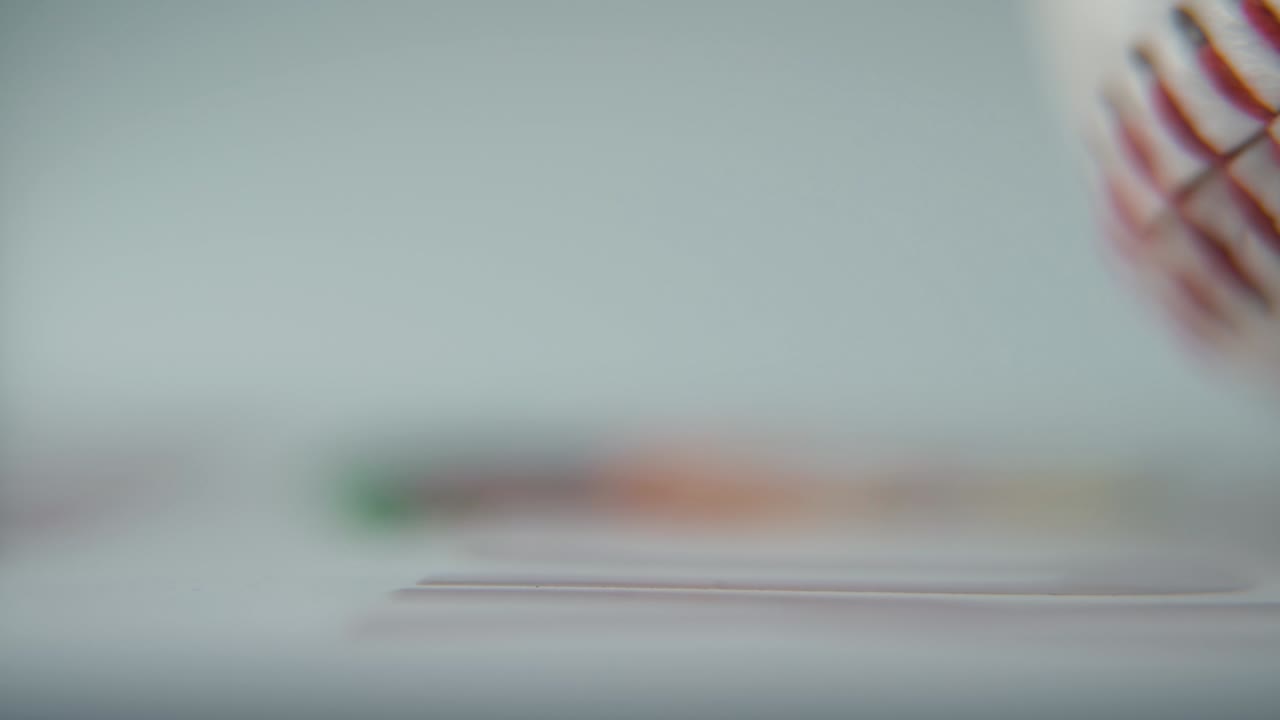 Macro inquadratura cinematografica commerciale di una palla da baseball bianca che ruota, primo piano sulle cuciture rosse, illuminazione professionale da studio, slow motion fluido a 120 fps