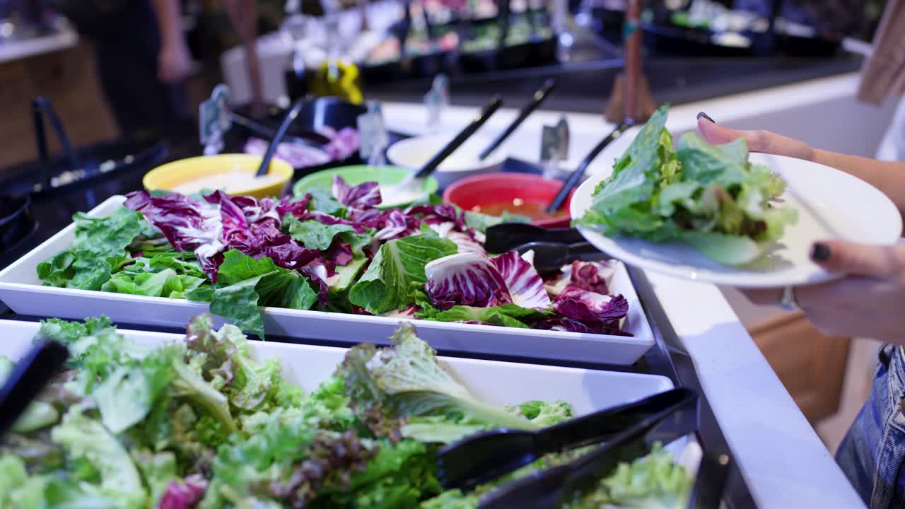 Close-up of woman selecting leafy greens at salad buffet bar in bright restaurant lighting